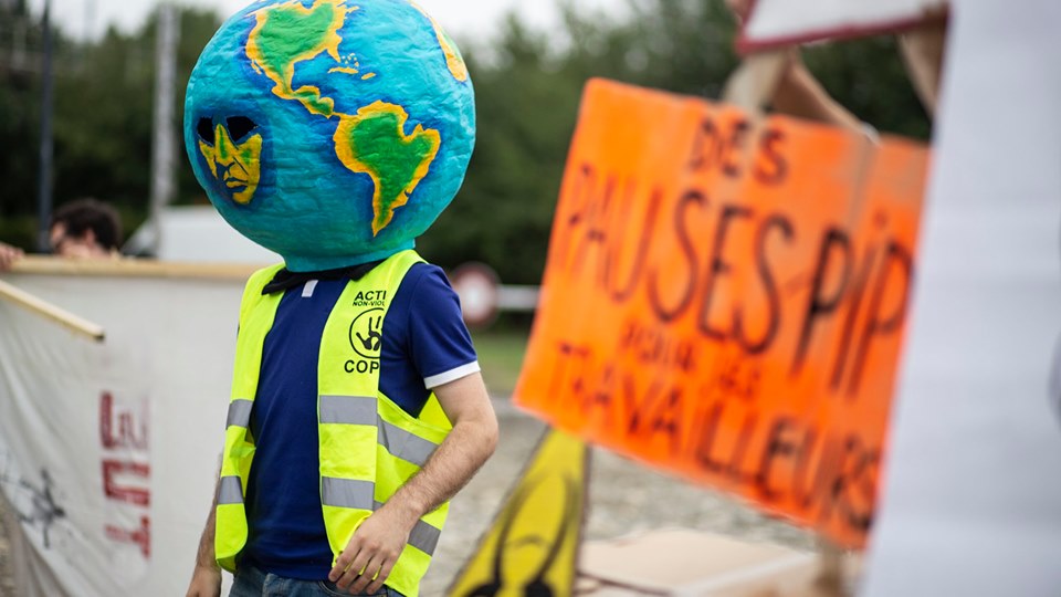 une personne avec un gilet ANV COP 21 et un masque de planète