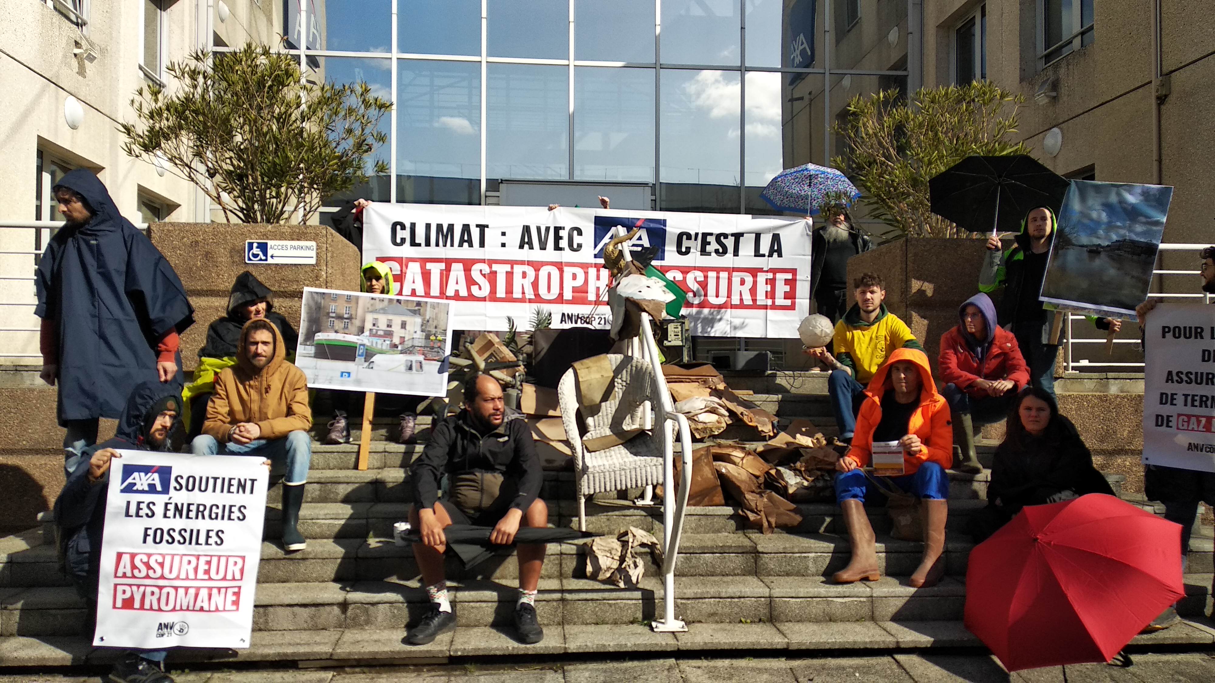 Des militant·es d'ANV-COP21 à Nantes ont déposé des débris provoqués par les inondations historiques de fin janvier en Ile-et-Vilaine devant une agence AXA pour dénoncer la culpabilité d’AXA dans le dérèglement climatique. Iles sont habillés avec des habits de pluies, tiennent des banderoles et des photos d'inondations. 