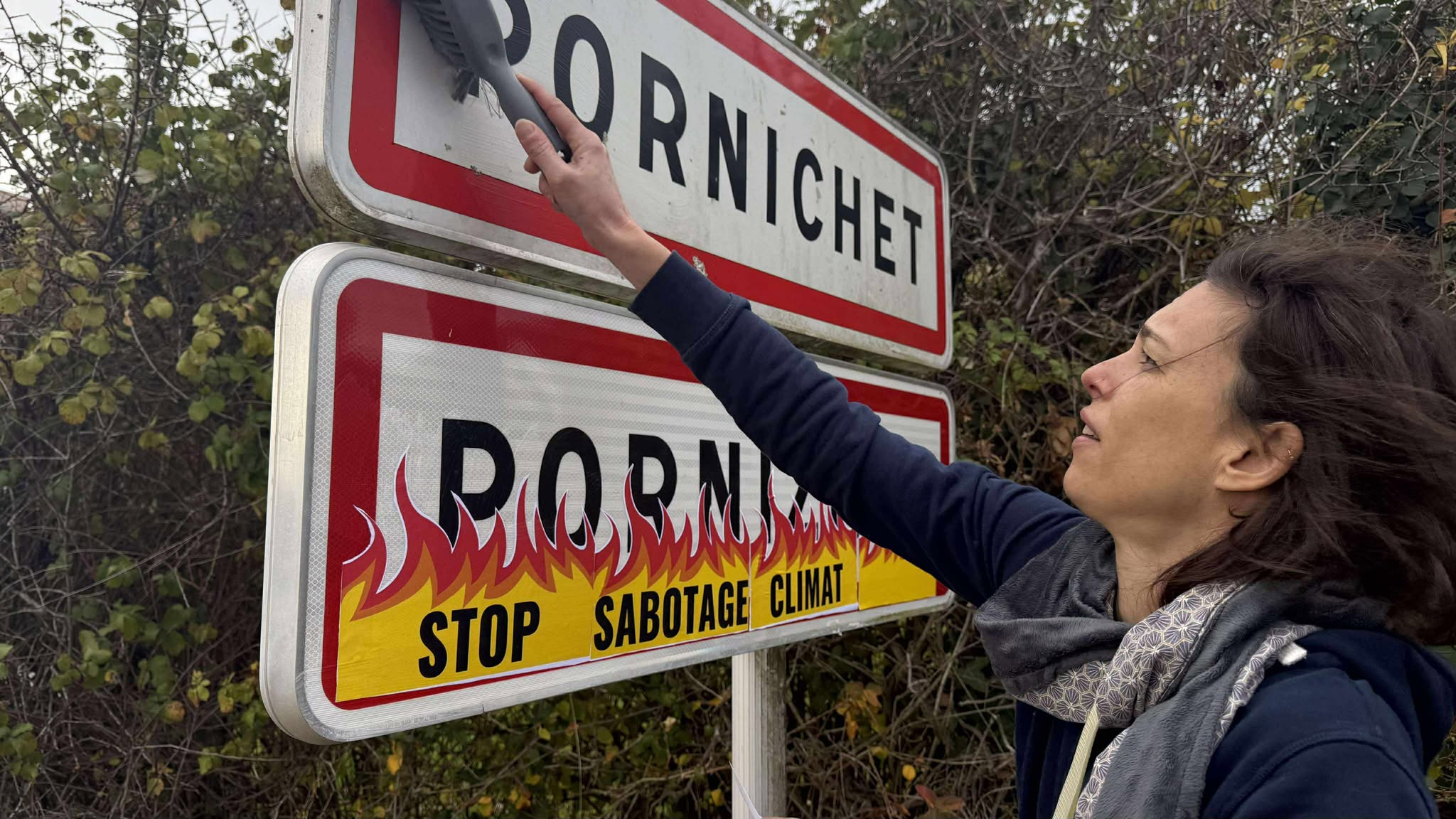 Une militante colle des flammes sur le panneau d'entrée de ville de Pornichet à l'aide d'un pinceau et de colle.