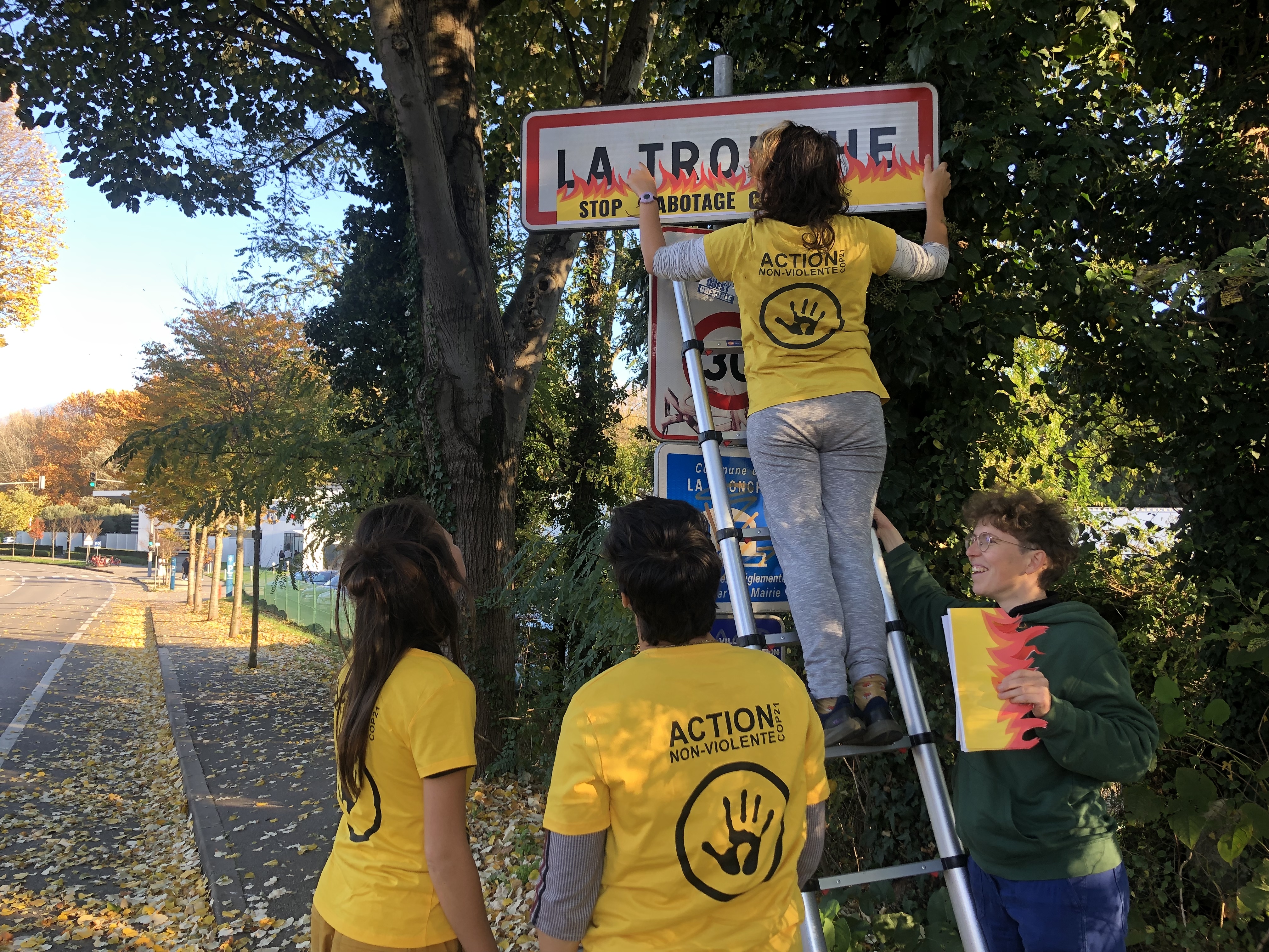 Des militantes d'ANV-COP21 collent des flammes sur le panneau d'entrée de ville de "La Tronche" à l'aide d'une échelle. 