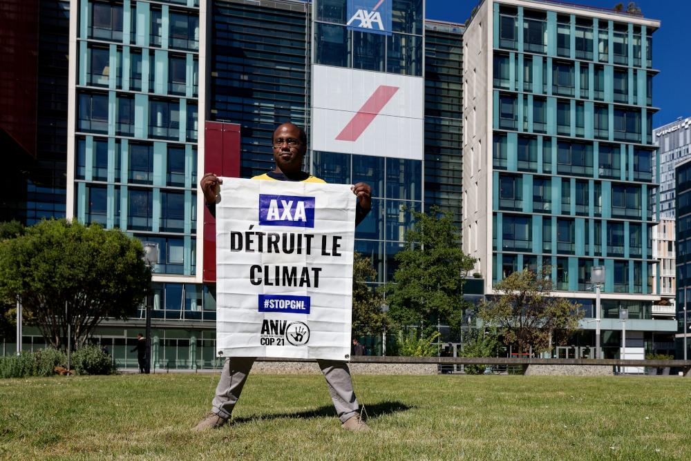 Un militant tient une banderole devant le siège : AXA détruit le climat